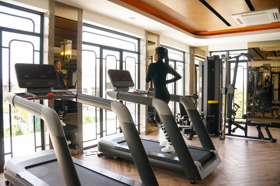 Young woman exercising on treadmill at a modern indoor gym with bright windows.