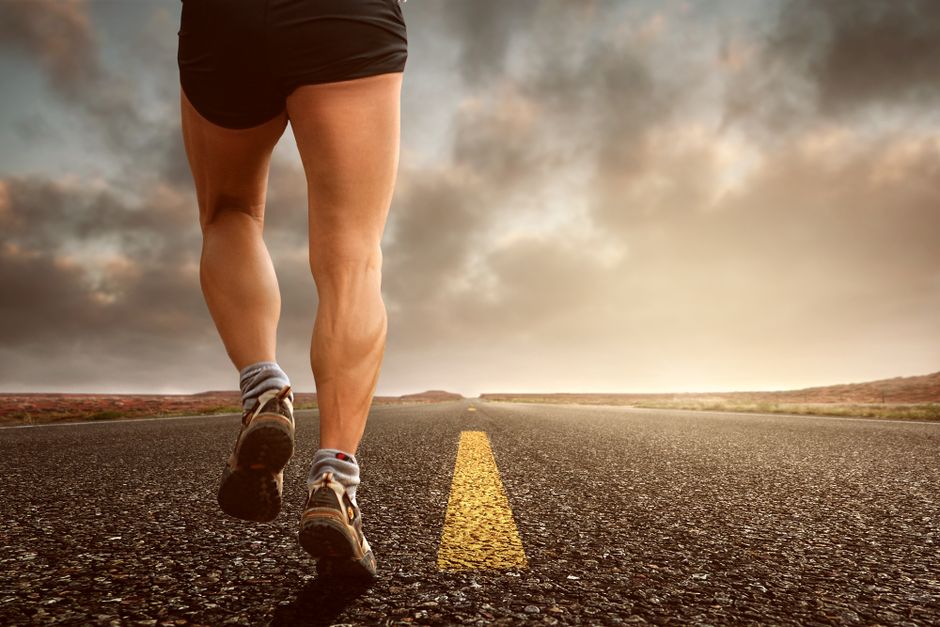 Runner's legs on a road during a sunset, symbolizing endurance and outdoor fitness training.